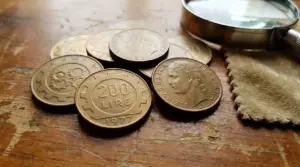 Monete da 200 lire del 1977 e 1978 su un tavolo di legno accanto a una lente d'ingrandimento
