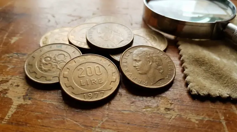 Monete da 200 lire del 1977 e 1978 su un tavolo di legno accanto a una lente d'ingrandimento